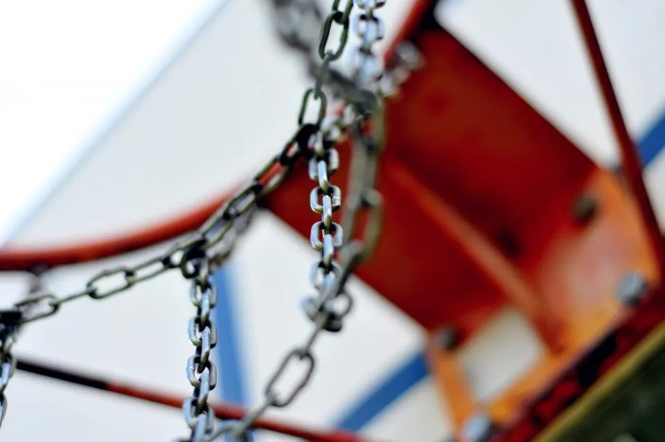 Detalle de un aro de baloncesto exterior con red de cadena y tablero blanco visto desde abajo
