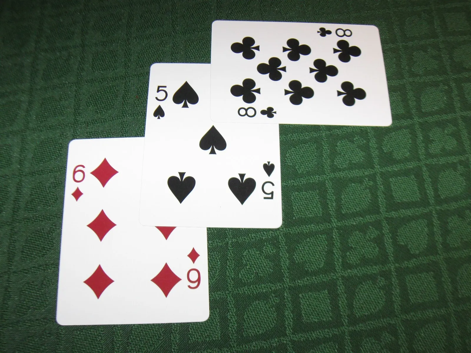 Tres cartas repartidas sobre un paño verde con dibujo geométrico en relieve