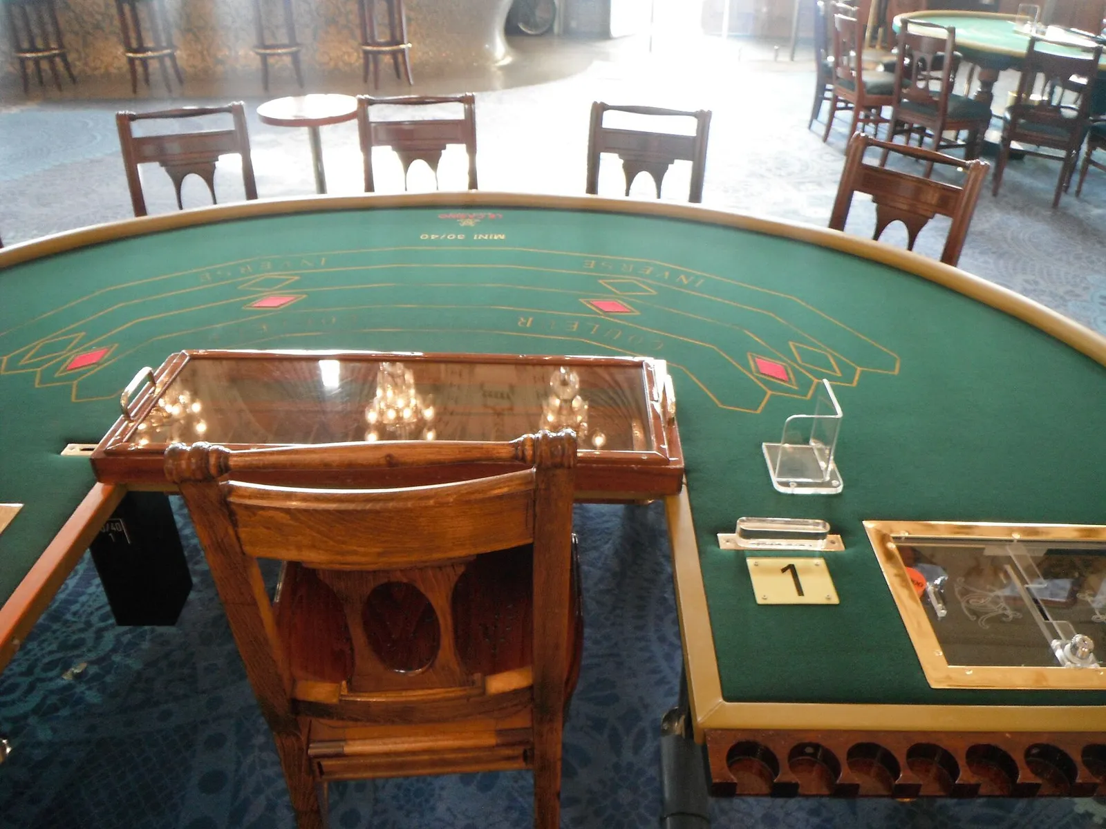 Mesa de casino de tapete verde con canto de madera barnizada y una silla de madera en el puesto del crupier
