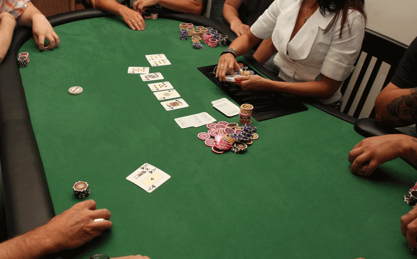 Tapete verde de una mesa de póker con cartas comunitarias repartidas, fichas apiladas y las manos de los jugadores