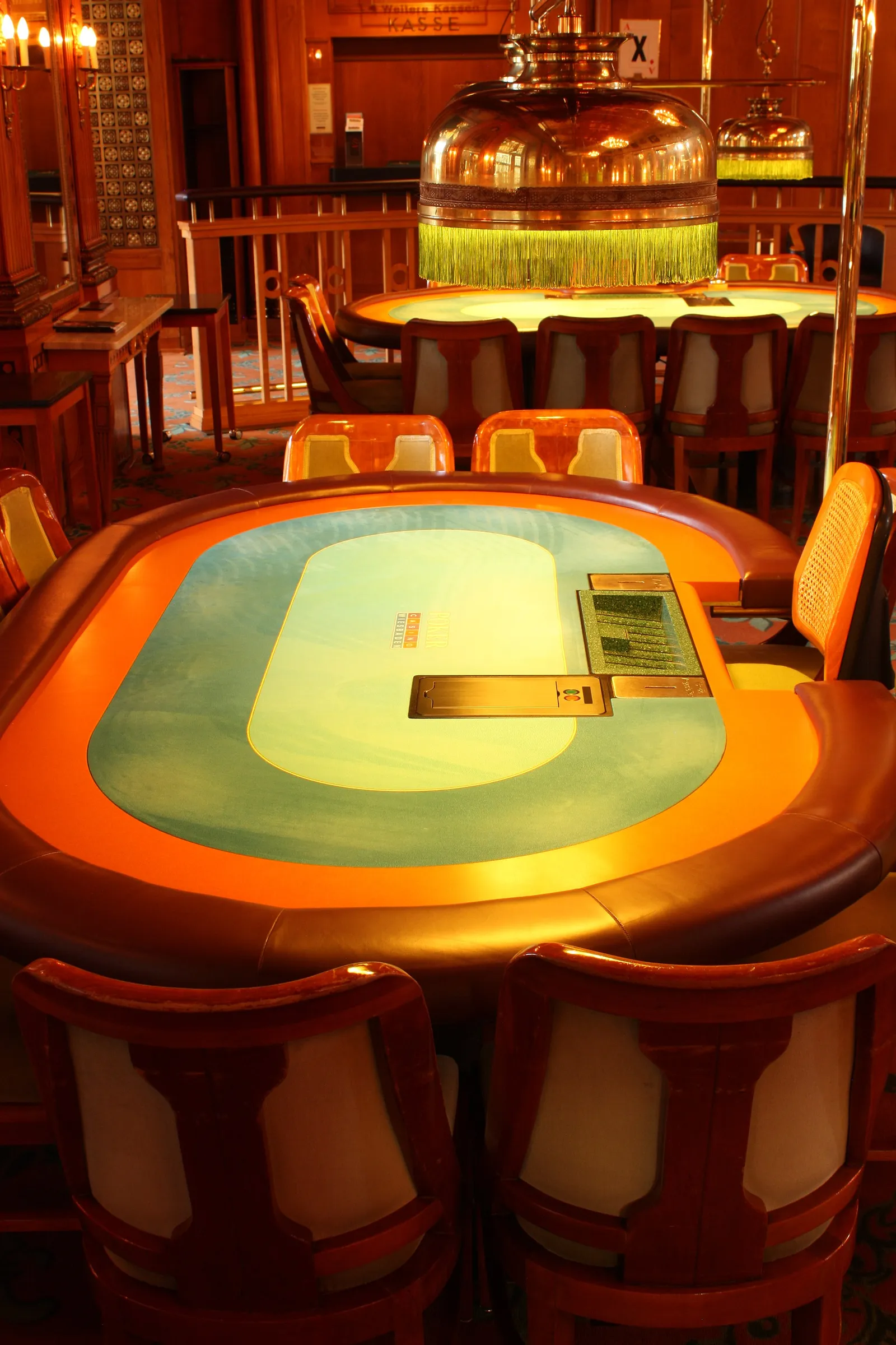 Mesa de póker ovalada con tapete claro iluminado y sillas de madera alrededor en una sala de casino