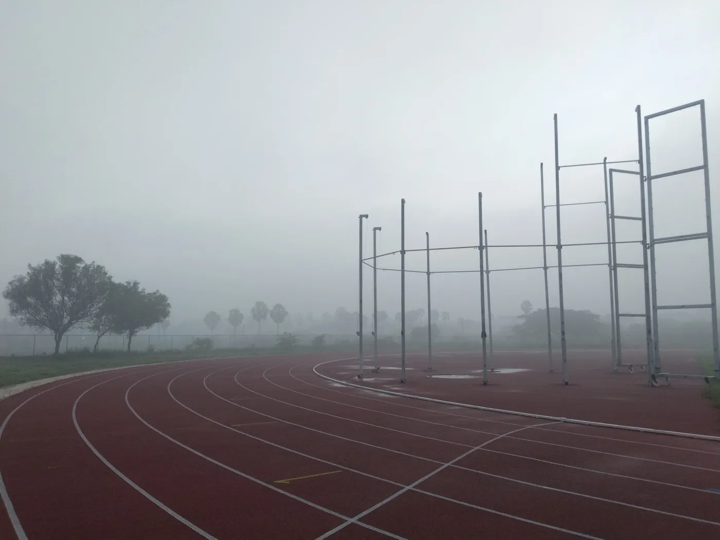 Pista de atletismo de tartán rojo entre niebla, con estructuras metálicas de la zona de lanzamientos