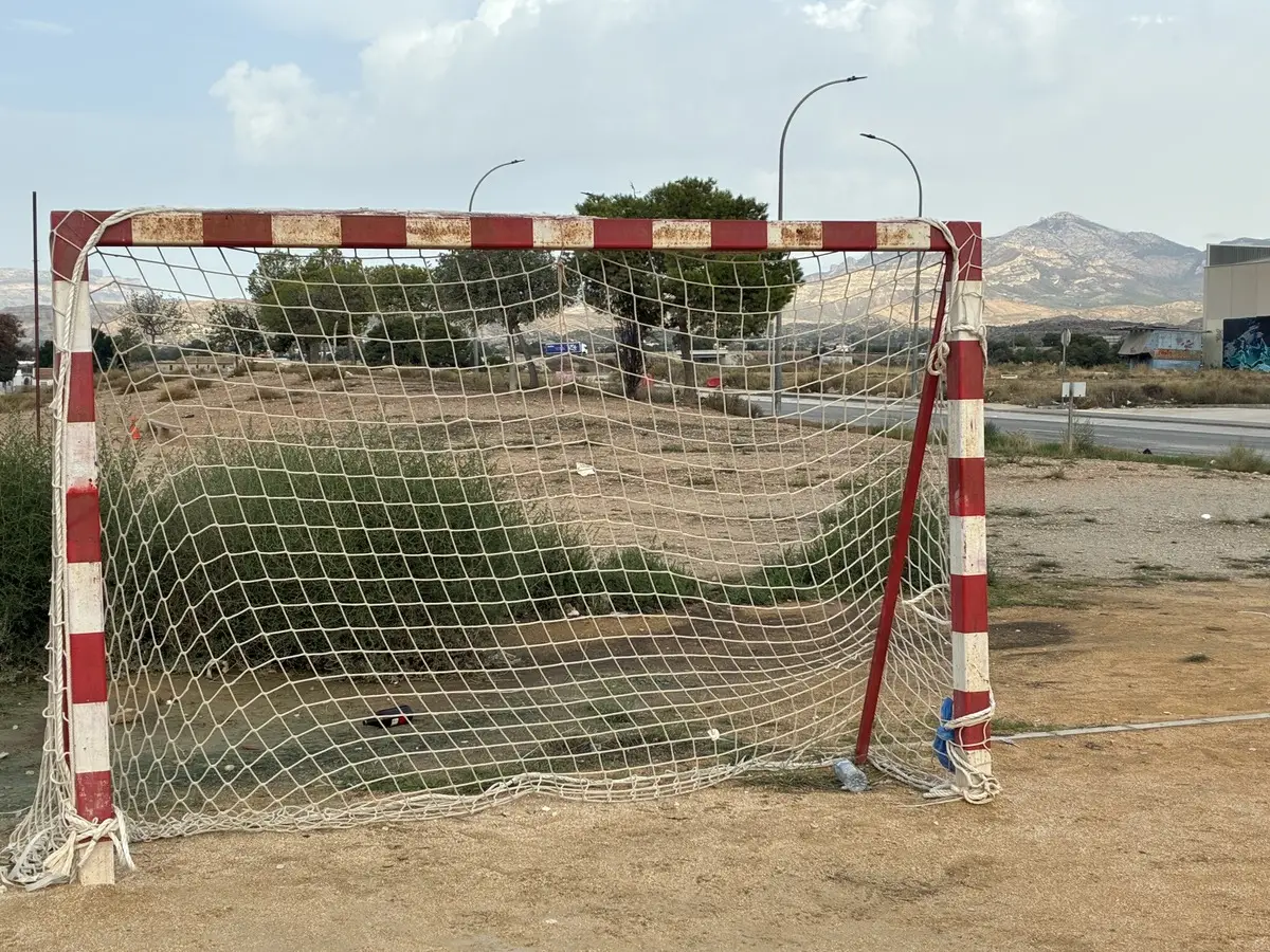 Portería de fútbol sala con postes a franjas rojas y blancas en una pista exterior de tierra