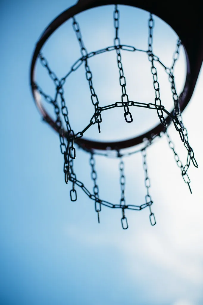 Aro de baloncesto con red de cadena visto en contrapicado contra un cielo azul con nubes