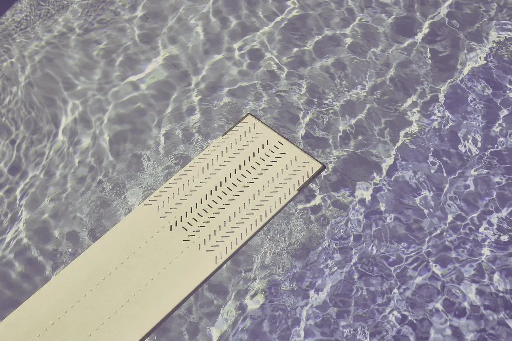 Trampolín claro sobre el agua de una piscina con reflejos y ondulaciones en la superficie